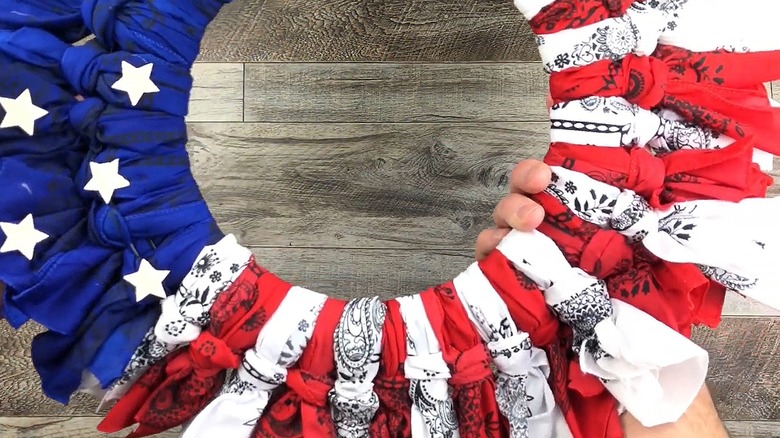 A patriotic wreath is made out of blue, red, and white bandanas tied around a wire wreath form.