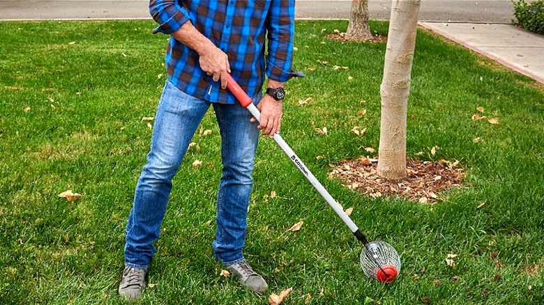 A person in blue flannel and jeans rolling the QuickCollector over their grass