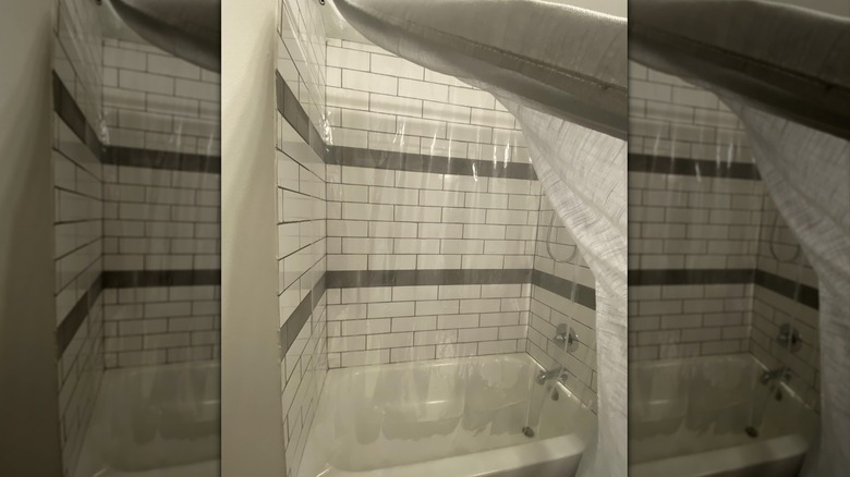 clear shower liner in a bathtub with white tiles