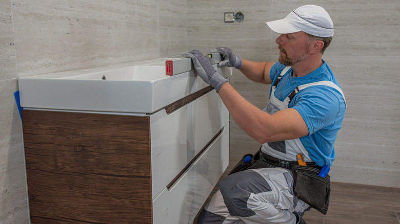 A contractor checks the stability of a newly installed bathroom vanity with a level.