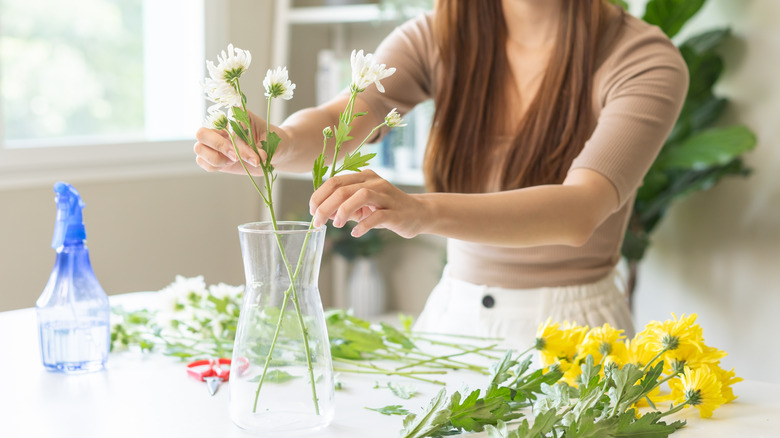 Woman adding flowers to a plain glass vase