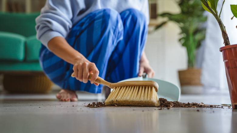 Person sweeping up spilled dirt with a handheld broom and dustpan