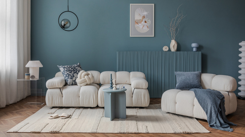 A blue walled living room with cream sofas, a large rug and painted blue radiator, with a small blue table used as a coffee table.