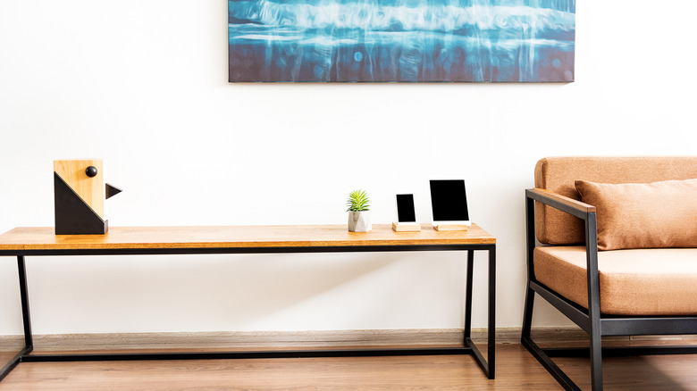 A slim bench used as a table alongside a sofa with an iPad and iPhone on stands on it, along with a very small house plant.