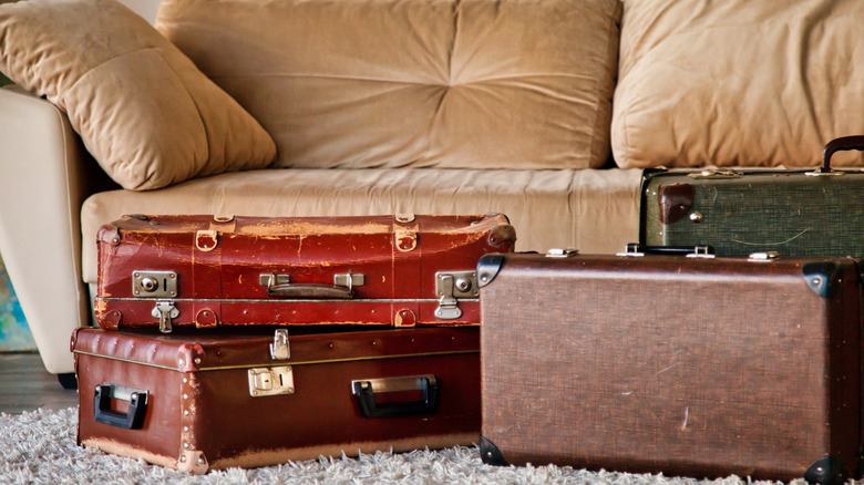 Old suitcases stacked on the floor in front of a sofa.