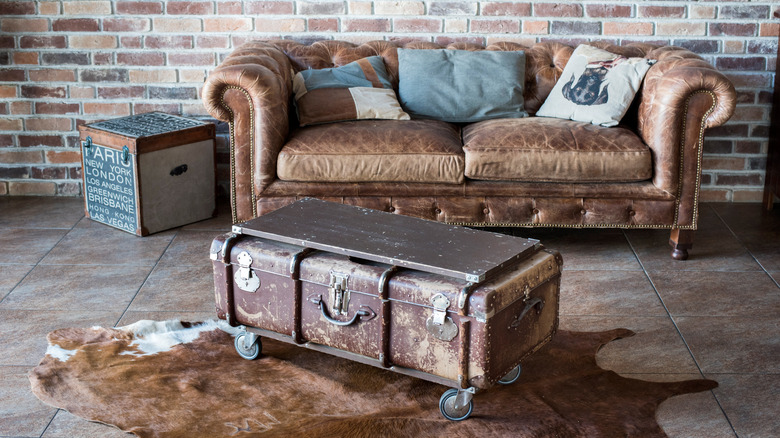 A utilitarian apartment with brick walls, a battered Chesterfield sofa and a vintage trunk in front of it used as a table.