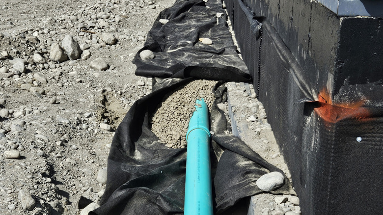 a French drain installation with non-woven fabric wrapped around clean rock and a perforated pipe