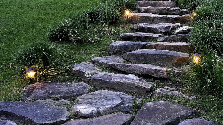 A stone walkway in a backyard illuminated by small torch lights