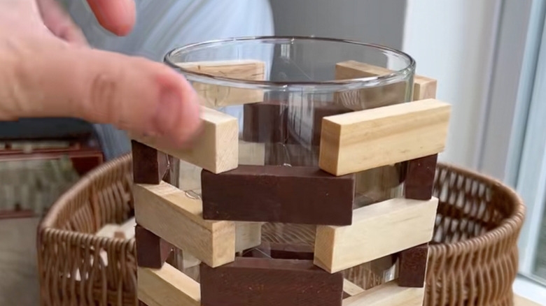 woman putting wooden blocks on a glass vase
