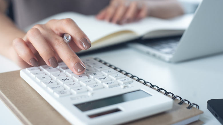 Woman's hand on a calculator with a pen and a laptop