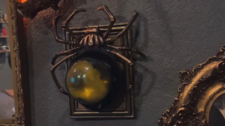 A glowing spider made from Dollar Tree supplies hangs on a wall on a frame.