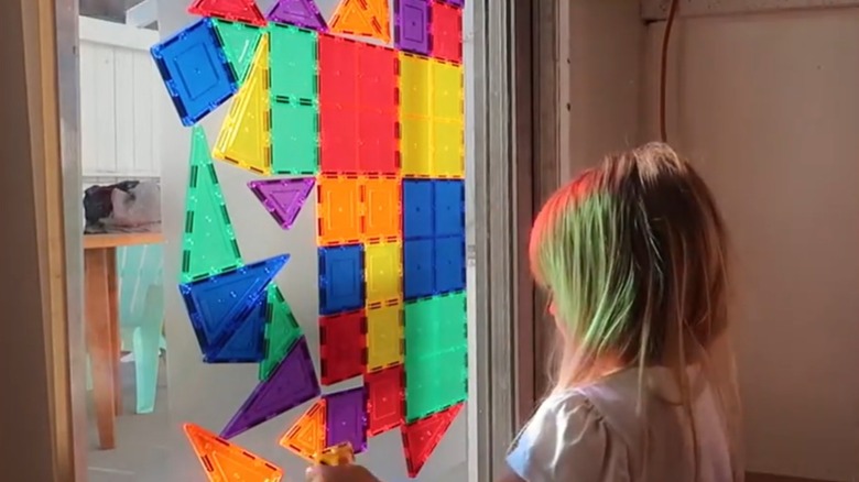 A blonde child arranges magnetic blocks on a sticky window surface.