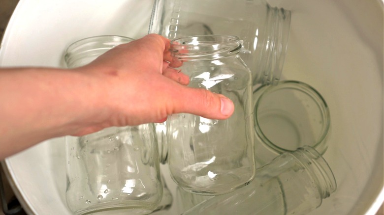 Person pulling empty glass jar from bin for repurposing