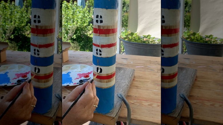 Woman painting tree log to resemble lighthouse