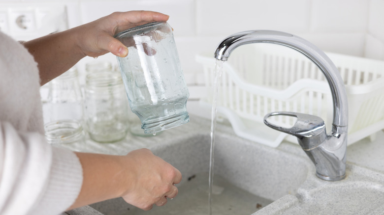 A woman cleans an empty pickle jar in the kitchen sink.