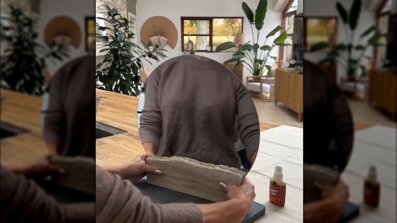 A woman glues two travertine slabs to either side of a round IKEA mirror.