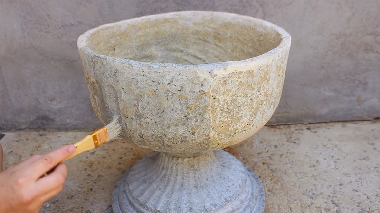 Person brushing sealer onto concrete planter.