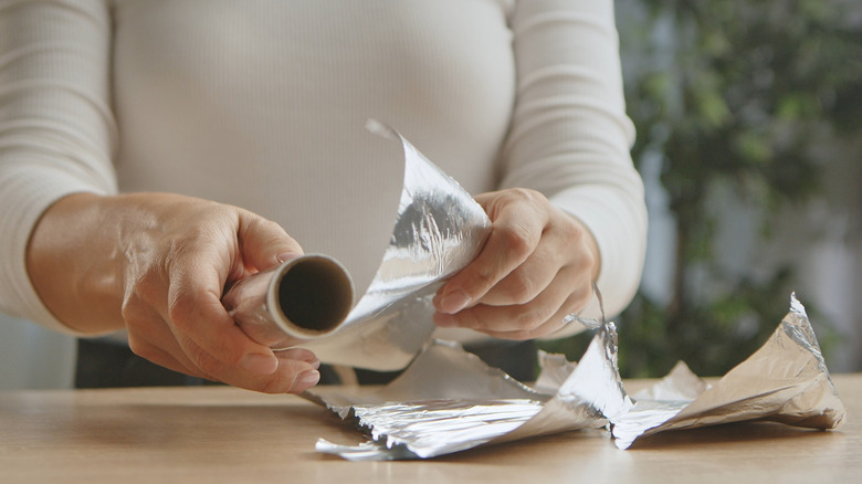 Woman's hand ripping sheets of aluminum foil off of roll