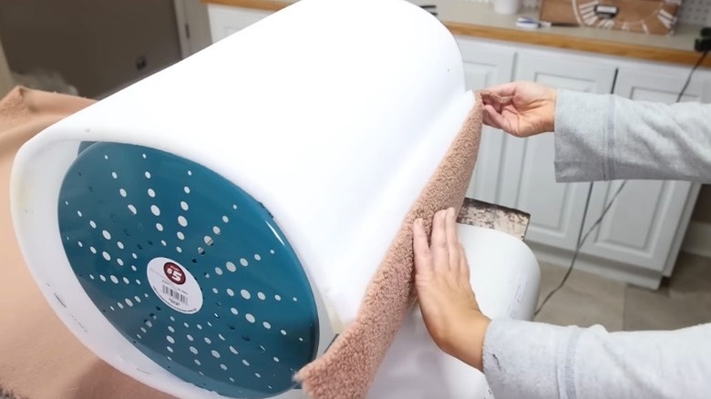 Woman wrapping Dollar Tree stool with foam and fabric to make DIY ottoman