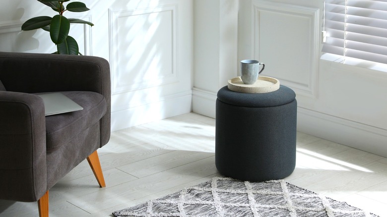Charcoal ottoman holding tray with mug near armchair