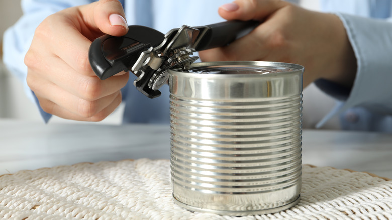 Woman opening tin with can opener at table, closeup
