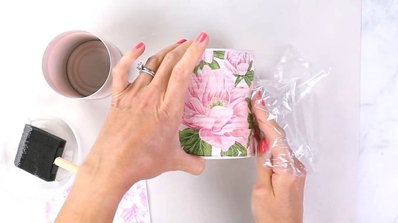 A woman uses a napkin to decorate a tin can