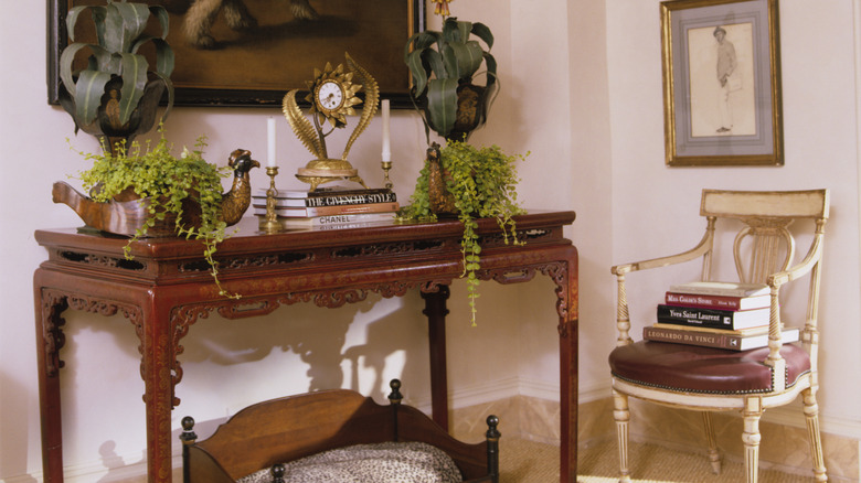 Vintage wooden entryway table with ornate details, decor and books on top of the table.