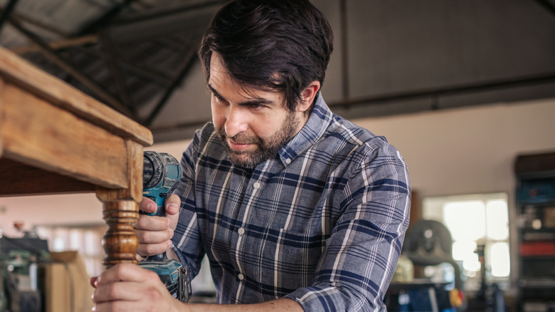 A man attaches legs to a wooden bench using a drill.