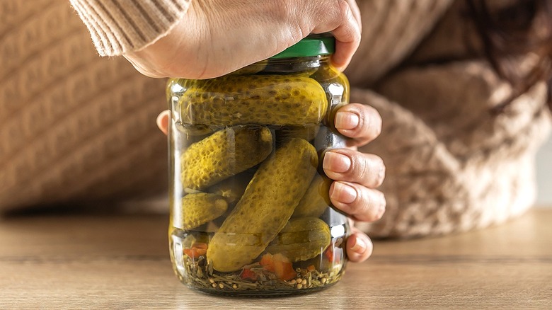 Close-up of a person twisting the lid off of a jar of pickles