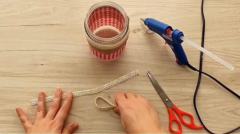 Demonstrator preparing lace ribbon for placement on an empty jar, a glue gun and pair of scissors are seen on the right