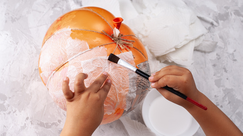 Child's hand making a paper mache pumpkin
