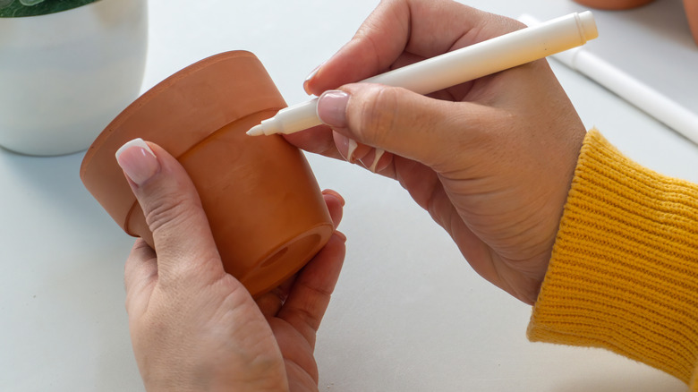 Person's hands decorating clay pot with marker