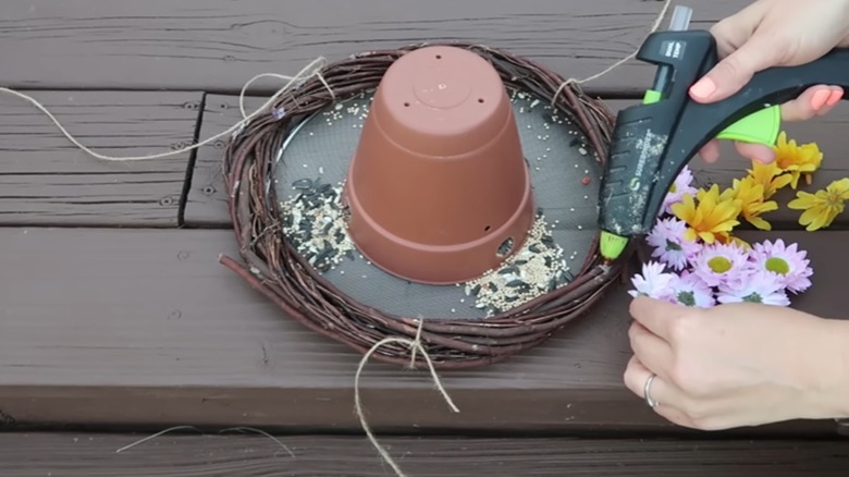 demonstrator building DIY feeder with terracotta pot, wreath, and glue gun on wood table