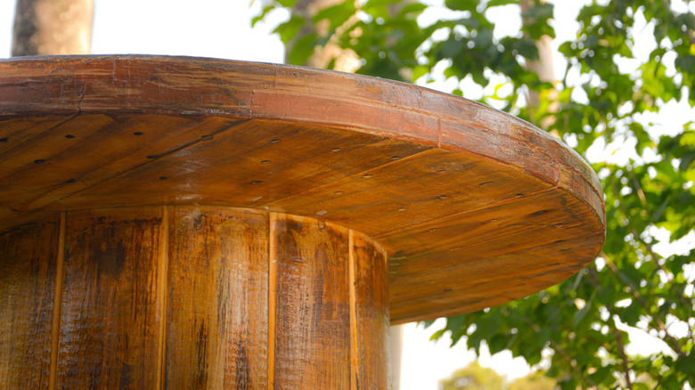 A wooden spool table with a rustic looking finish with tree in background