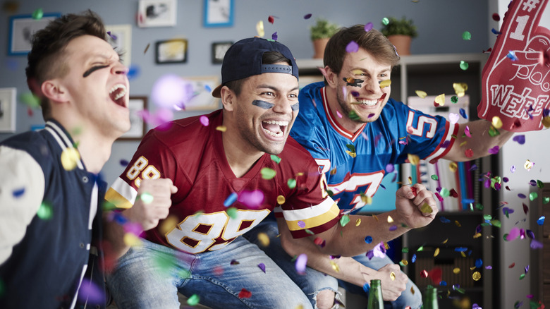 Three men cheering watching football