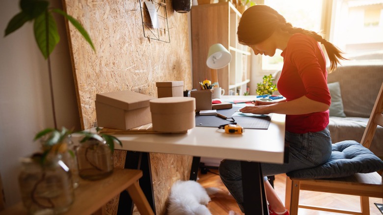 Woman crafting at table with square and round cardboard boxes.