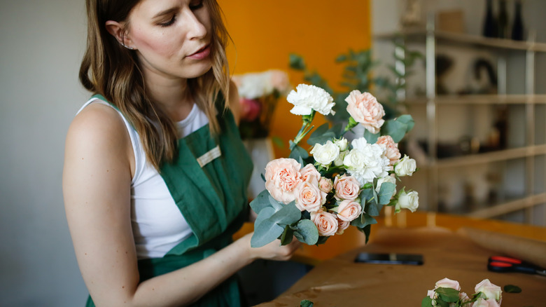 A woman in a green apron arranging an assortment of white and pink faux flowers.