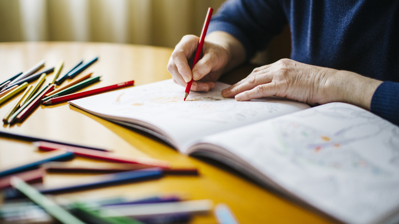 A person using pencils to color in a coloring book