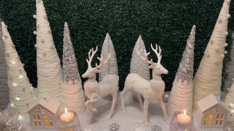 A series of white yarn and glittery Christmas tree cones with two white stags in the center