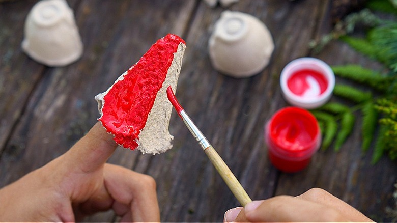 The pointed section of an egg carton rests on someone's finger while it's being painted red