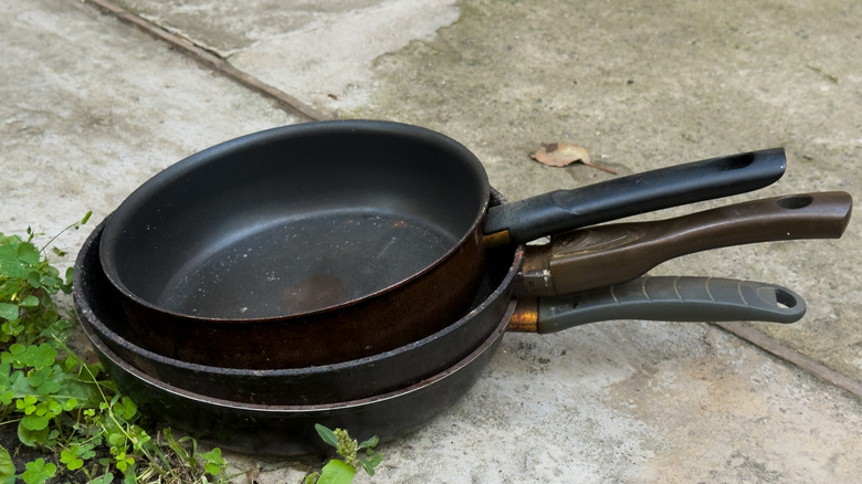 Three stacked teflon frying pans sitting on concrete