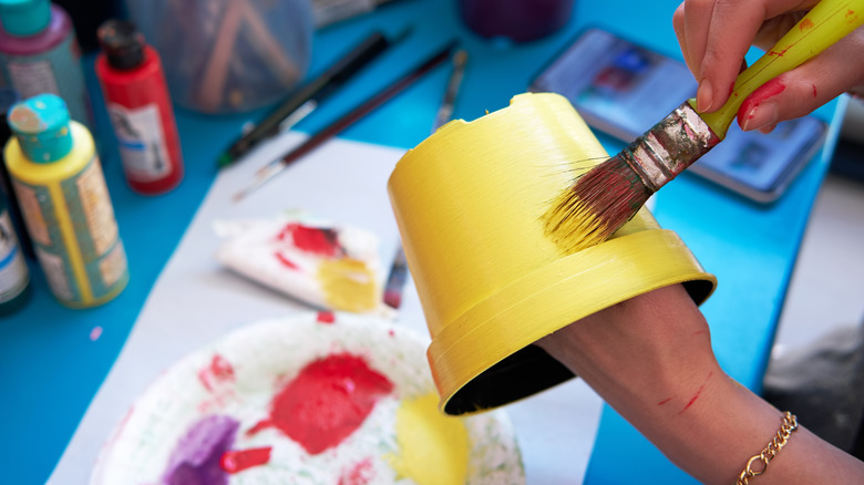 A person paints the exterior of a plastic nursery pot yellow.