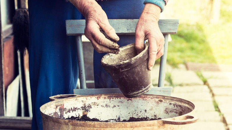 A gardener takes soil out of an old plastic plant pot in order to use it for a DIY project.
