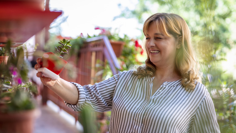 Woman in a striped shirt arranging potted plants on an outdoor balcony