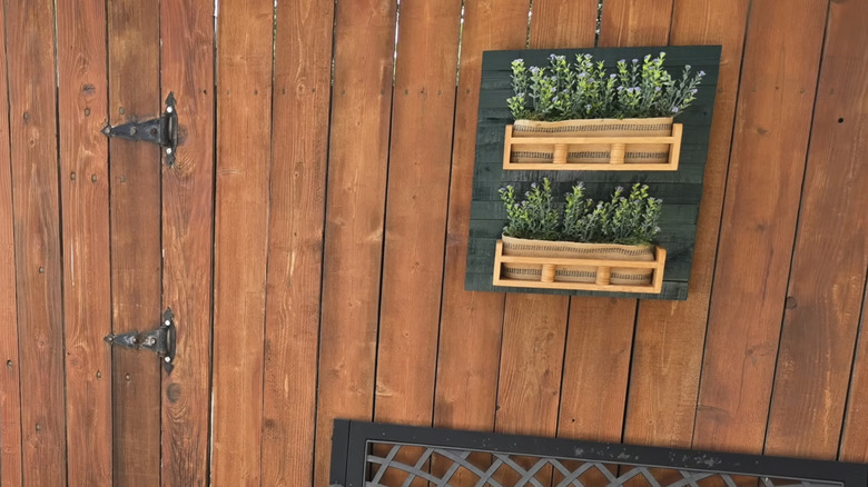 A fence with two spice racks full of artificial flowers hanging from a painted wooden board