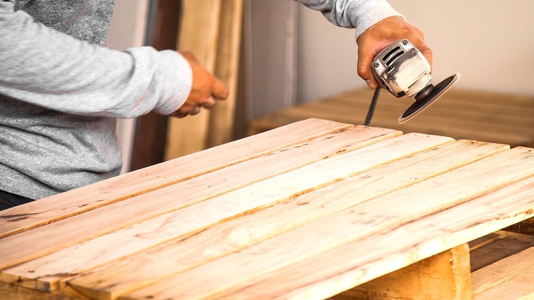 Close-up of a person holding a rotary tool near a wooden pallet