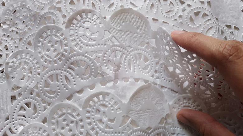 A person lifts a white paper doily from a stack.