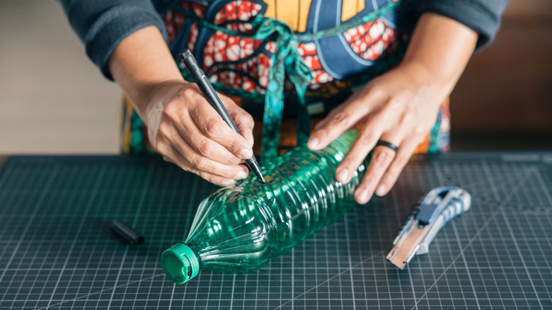 A person draws on an empty plastic soda bottle with a black marker.