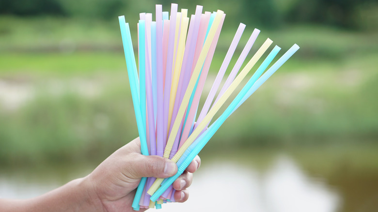 A child's hand holds a cluster of multicolored pastel bendy drinking straws.