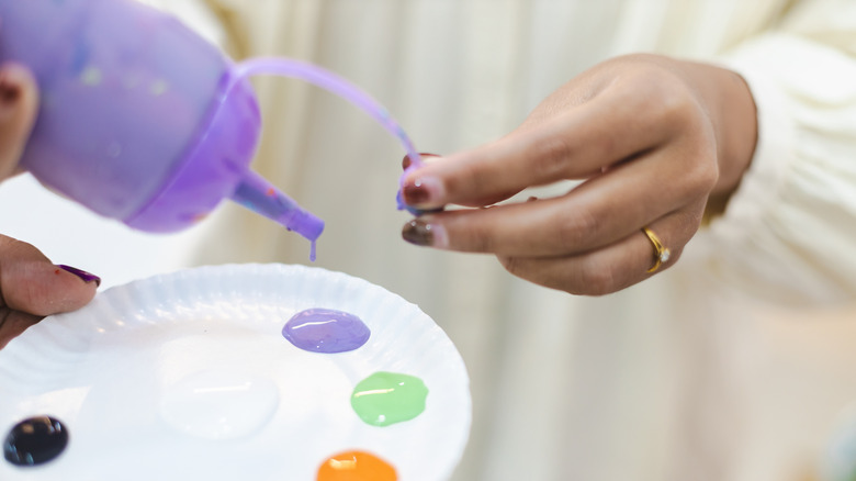 A person pours purple paint into a plastic palette